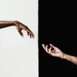 Two hands reaching across a stark black and white divide, symbolizing connection and unity.